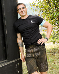 Hodalump-Lederhose für Herren aus dunklem Wildleder mit traditioneller Stickerei, getragen im Outdoor-Ambiente.
